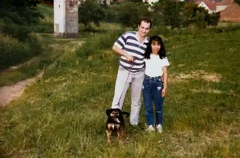 Tony and Tomoko standing outdoors with Lady in Melbach, Germany, with fields and hills behind them.